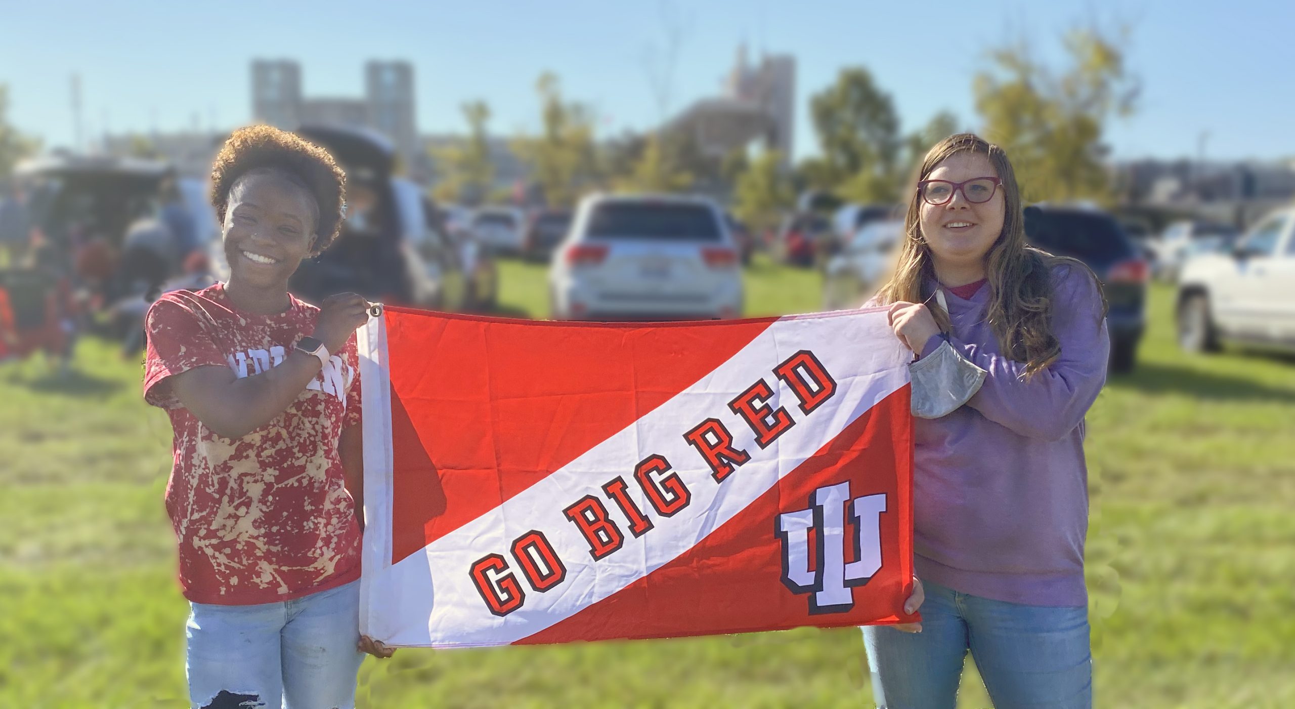 Two students smiling holding a "go big red' Banner